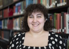 Gabby Hudziak in black and white polka dot shirt stands in front of library stacks.
